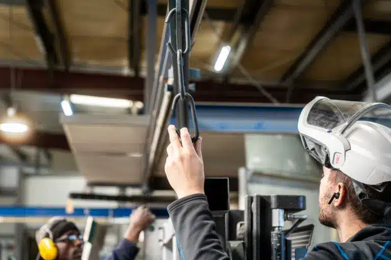 Zwei Mitarbeiter von KBN beim Teamwork vor der Strahlkabiene mit großem Industriebwerkstueck.