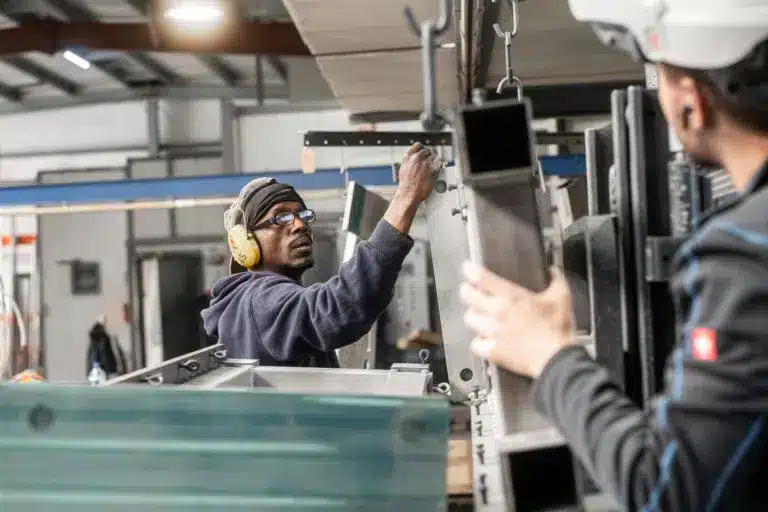 Zwei Mitarbeiter von KBN beim Teamwork vor der Strahlkabiene mit großem Industriebwerkstueck.